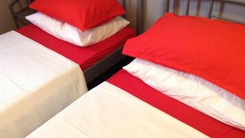 Two single beds with red and white bedding, metal headboards, and a red pillow on one bed.