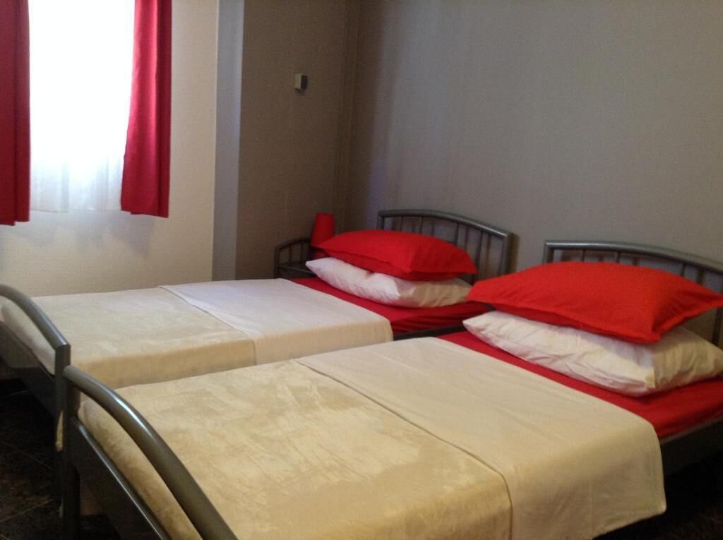 A room with two beds, each with a red pillow and a white pillow, and a window with red curtains.