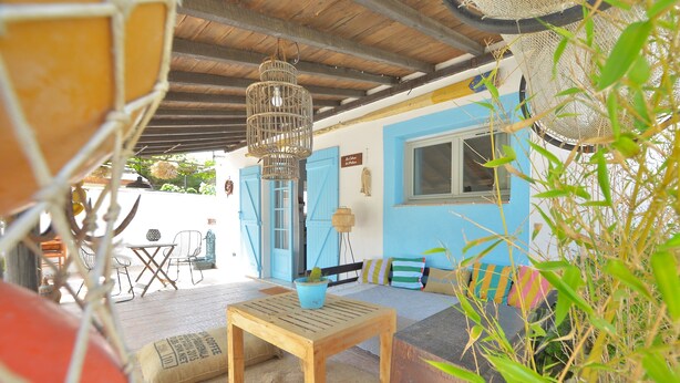 Un espace de détente extérieur accueillant, avec une table et des chaises en bois, un canapé bleu et un luminaire suspendu.