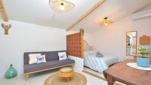 Une pièce chaleureuse avec un canapé, une table à manger, un petit tabouret, un tapis tissé, un cactus et un miroir au mur.
