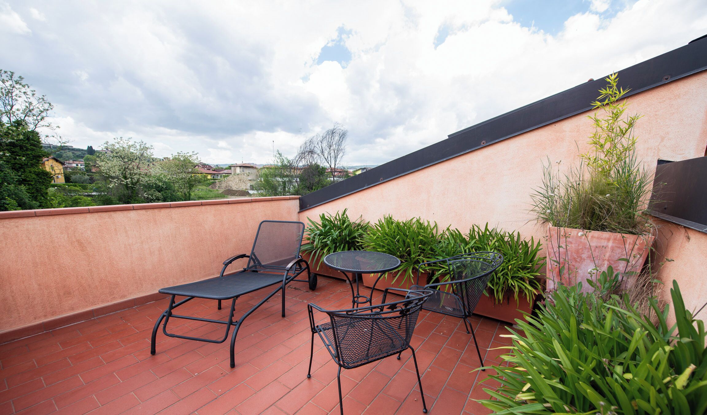 Eine Dachterrasse mit zwei Stühlen und einem kleinen Tisch, umgeben von Blumentöpfen und Blick auf die Stadtlandschaft.