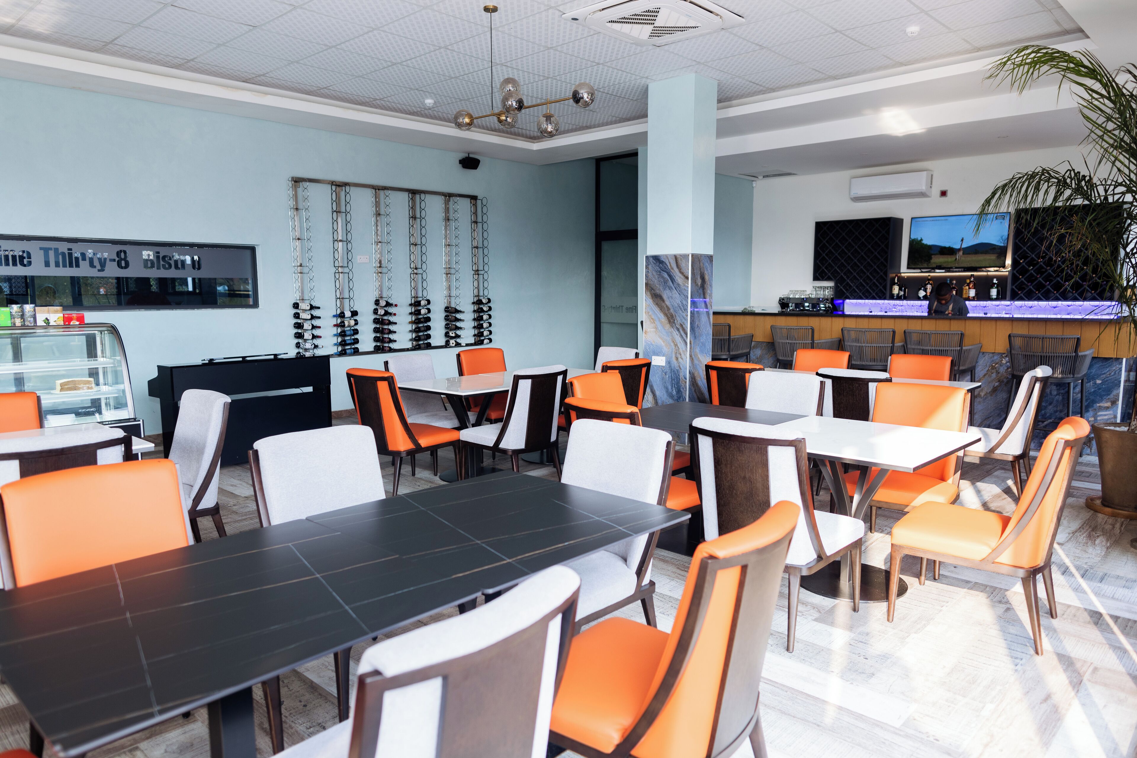 Ein modernes Restaurant mit mehreren Tischen, Stühlen, einer Bar und einem großen Bildschirm.