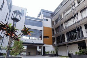 Un edificio moderno con techo plano, ventanas grandes y balcones. Hay plantas en macetas en primer plano.