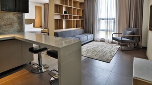 Ein modernes Wohnzimmer mit einer Couch, einem Sessel, einem an der Wand montierten Fernseher und einer eingebauten Bücherreolen.