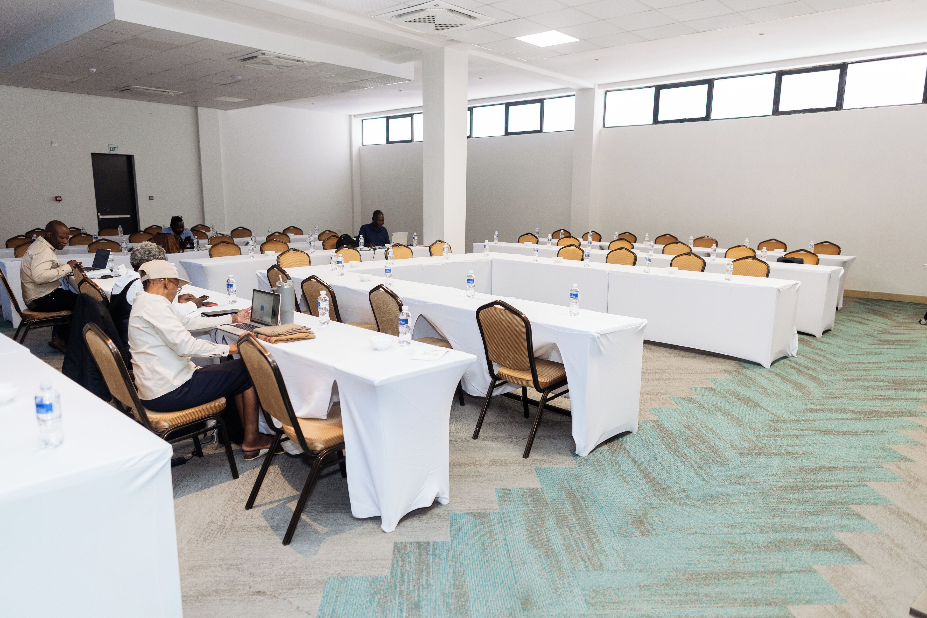 A conference room with long tables, chairs, and attendees.
