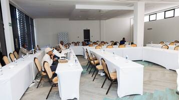 Un salón de conferencias con mesas largas, sillas y botellas de agua.