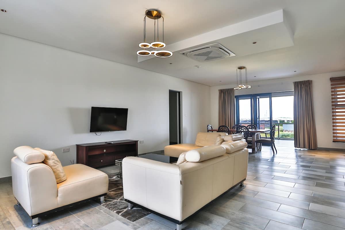 Una sala moderna con un sofá, sillones, un televisor de pantalla plana y un comedor con mesa y sillas.