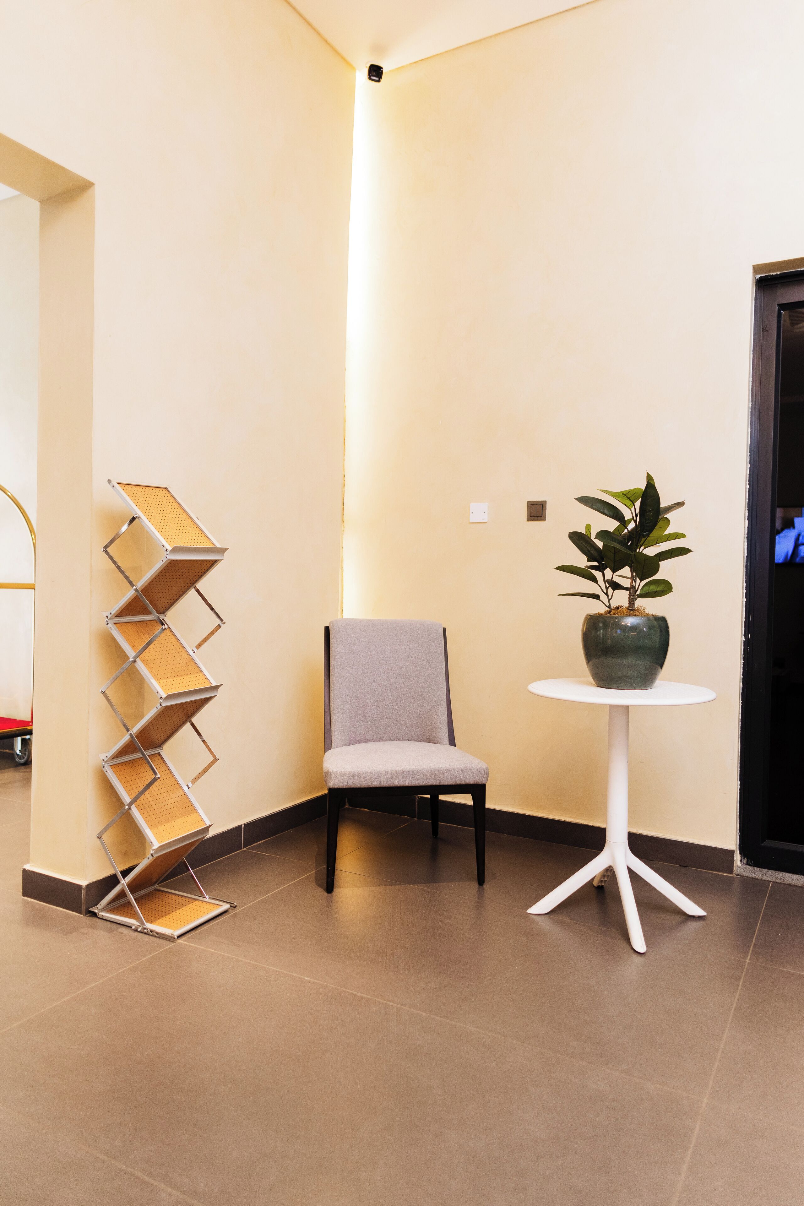 A modern interior with a grey chair, a white round table with a potted plant, and a metal rack against the wall.
