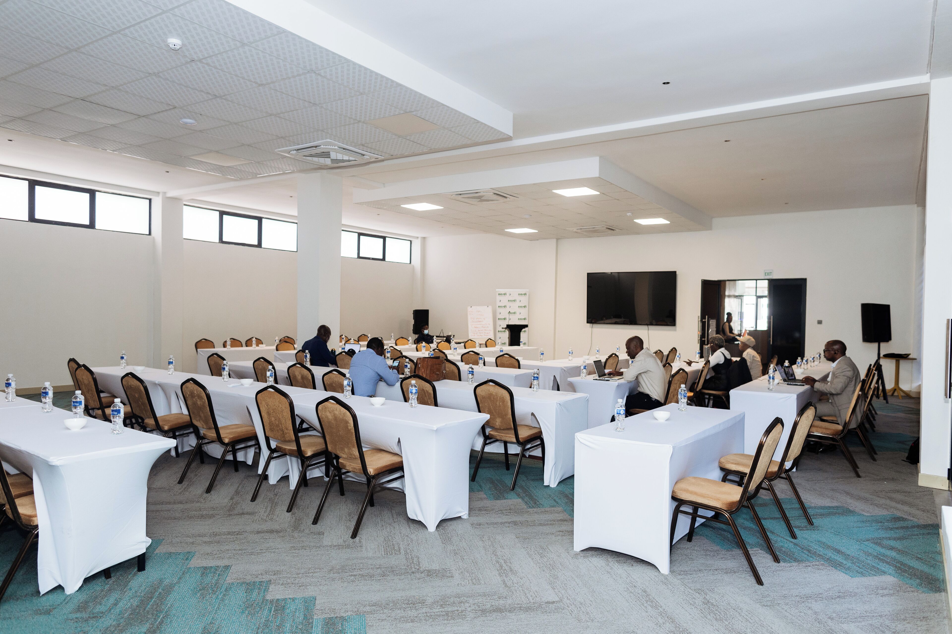 A conference room with multiple tables and chairs, equipped with water bottles and laptops.