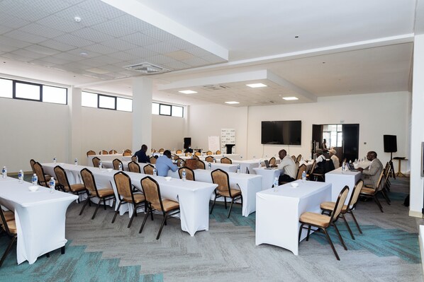 Un salón de conferencias con varias mesas y sillas, equipado con botellas de agua y portátiles.