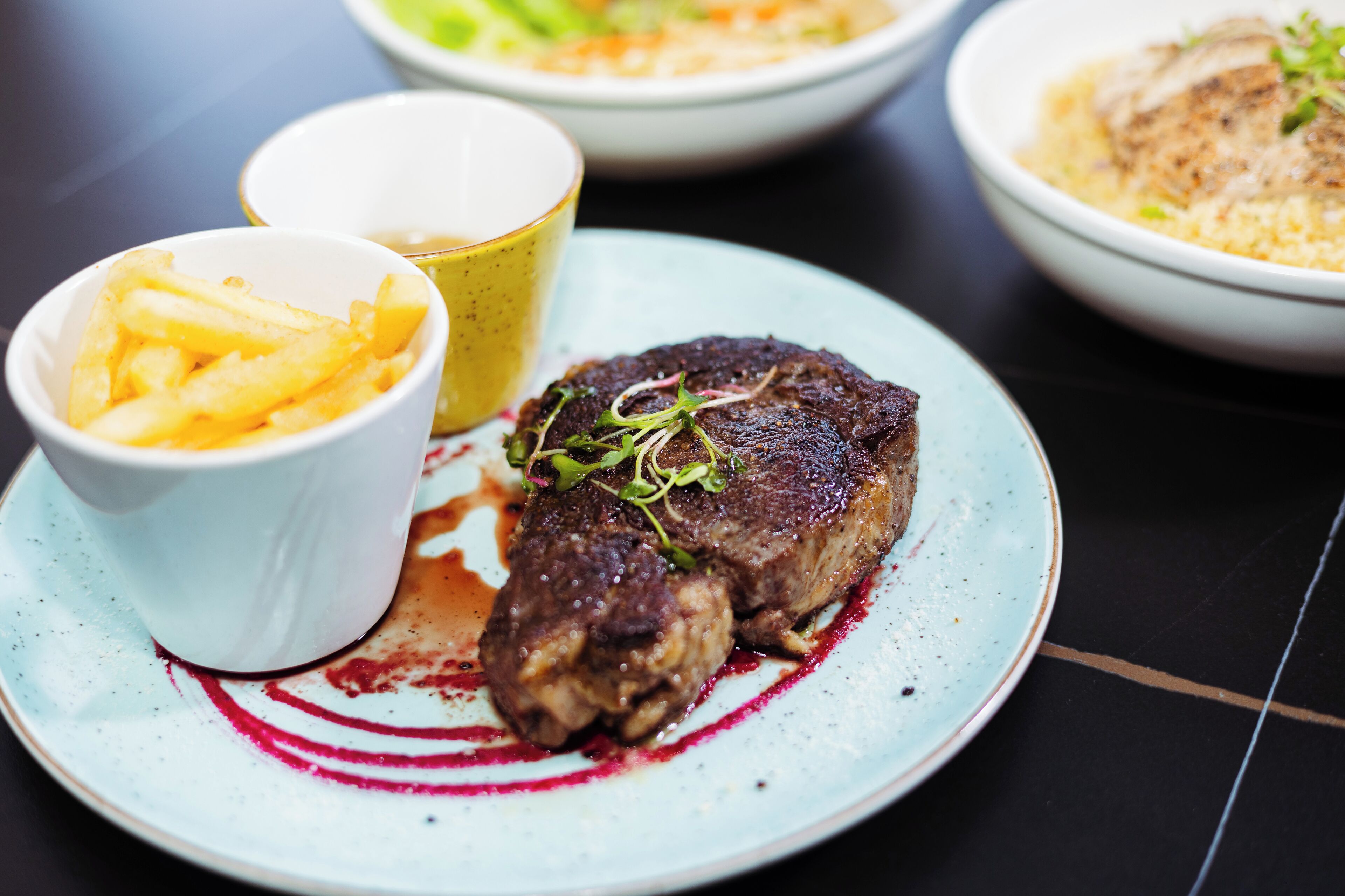 A plate with a steak, fries, and a cup of sauce.