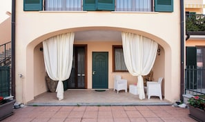 A building with a central entrance, a green door, and a covered porch with white chairs and a table.