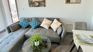 A modern living room with a grey sectional sofa, a glass coffee table with a plant, a dining table with chairs, a painting, and a mirror on the wall. - Cosy Apartment in the City Centre of Birmingham, walk to everything (Birmingham)