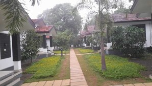 A pathway leading to a row of white buildings with red-tiled roofs, surrounded by greenery and palm trees. - Casita Lavender Resort (Vythiri)