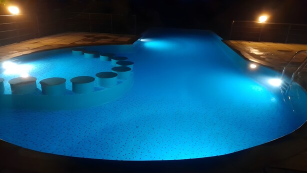 A swimming pool with a blue light, a deck, and a metal railing. - Casita Lavender Resort (Vythiri)
