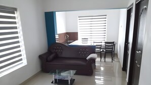 A modern living room with a brown sofa, a glass coffee table, and a dining area with a table and chairs. - Casita Lavender Resort (Vythiri)