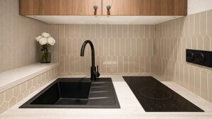 A modern kitchen with a black sink, stainless steel faucet, and a black induction cooktop. - Courtois (Paris)