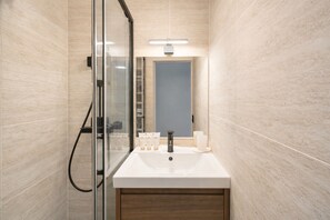 A modern bathroom with a glass shower enclosure, a white sink, and a mirror. - Courtois (Paris)