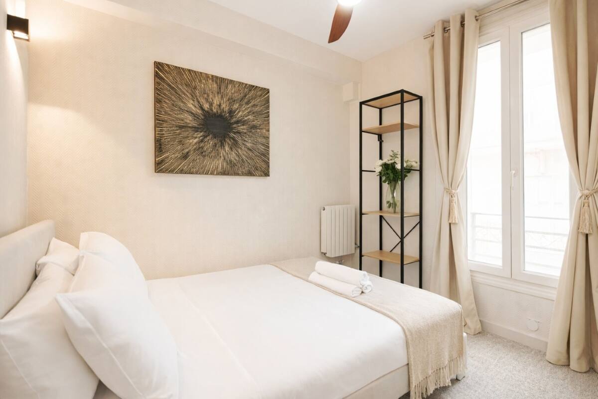 A bedroom with a bed, a radiator, a shelf with a plant, and a window with curtains.