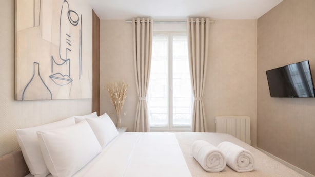 A hotel room with a bed, white bedding, a flat-screen TV, a window with curtains, and a painting on the wall. - Courtois (Paris)