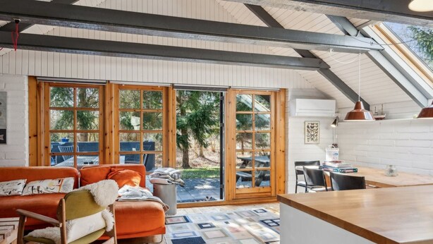 A cozy interior with a wooden ceiling, a large window, a sofa, and a dining area.