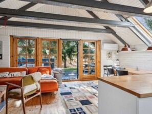 Un intérieur chaleureux avec un plafond en bois, une grande fenêtre, un canapé et un coin repas.