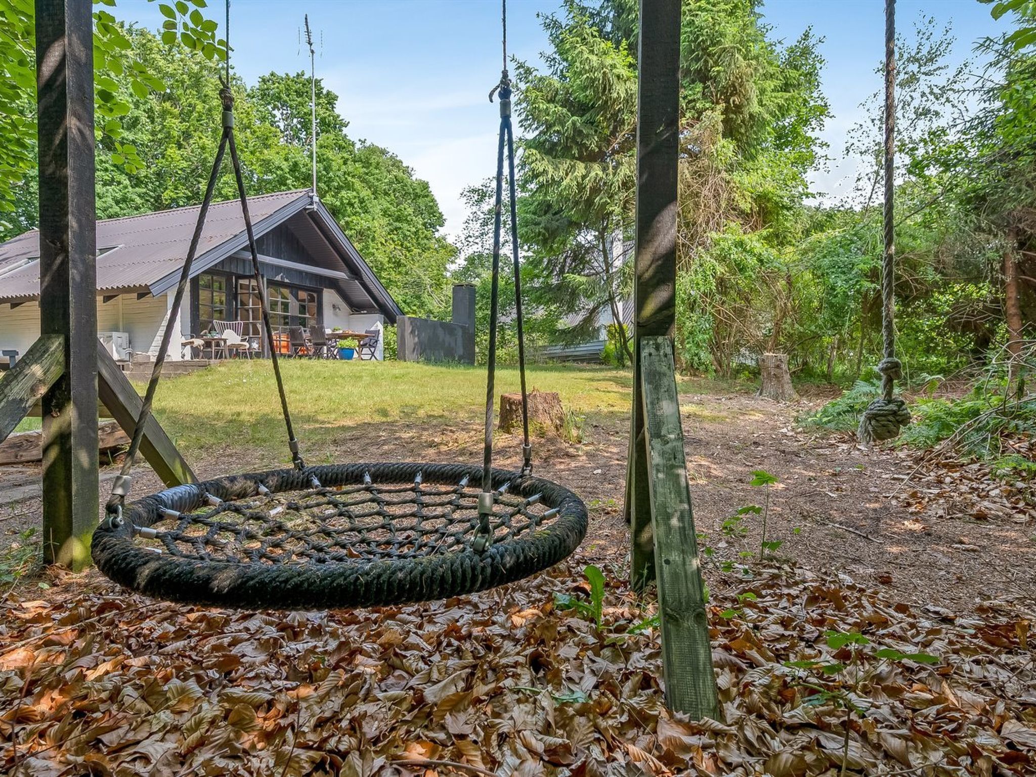 A wooden swing set in a wooded area with a house in the background.