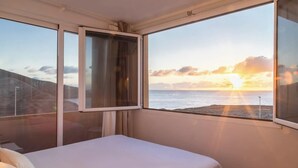Una habitación con cama y una ventana grande con vistas a un atardecer sobre el mar.