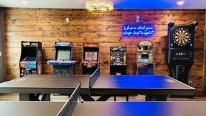 Una habitación con mesa de ping pong, juegos de arcade y dardos.