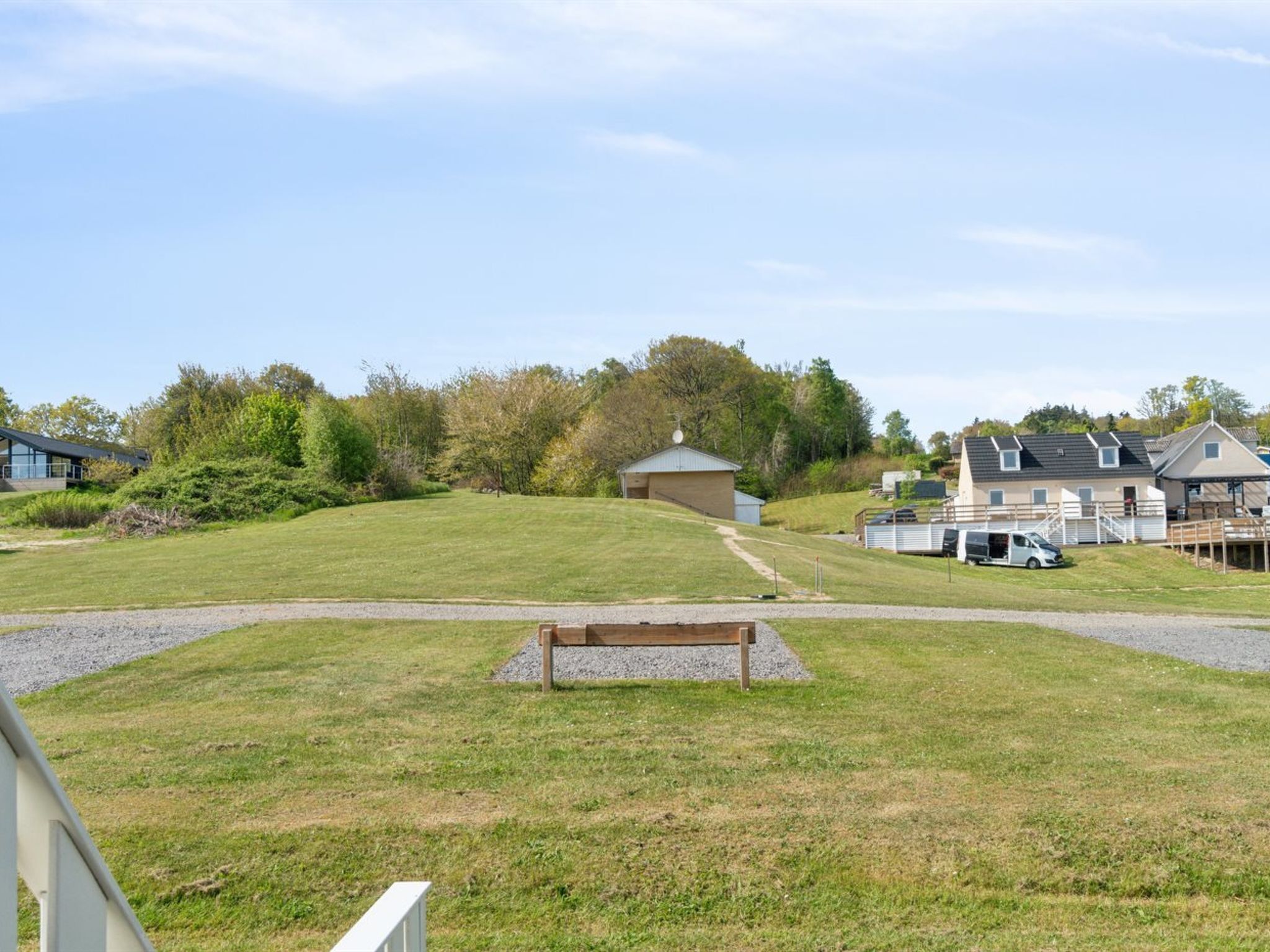 A grassy area with a bench, a small building, and several houses in the background.