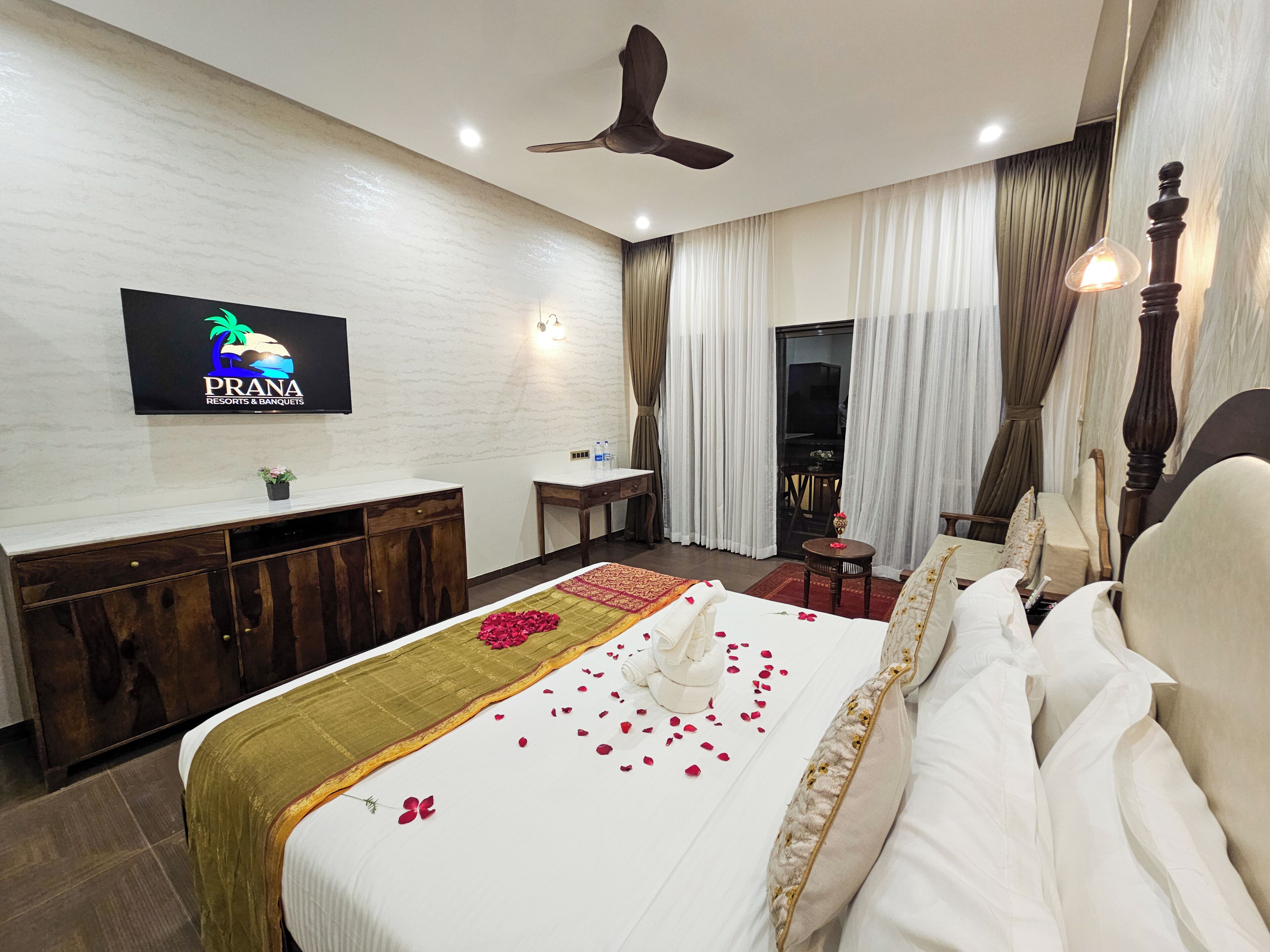 Una habitación de hotel con cama, escritorio, silla, televisor y ventilador de techo.