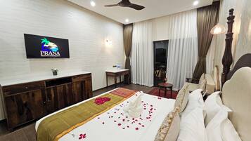 Una habitación de hotel con cama, escritorio, silla, televisor y ventilador de techo.