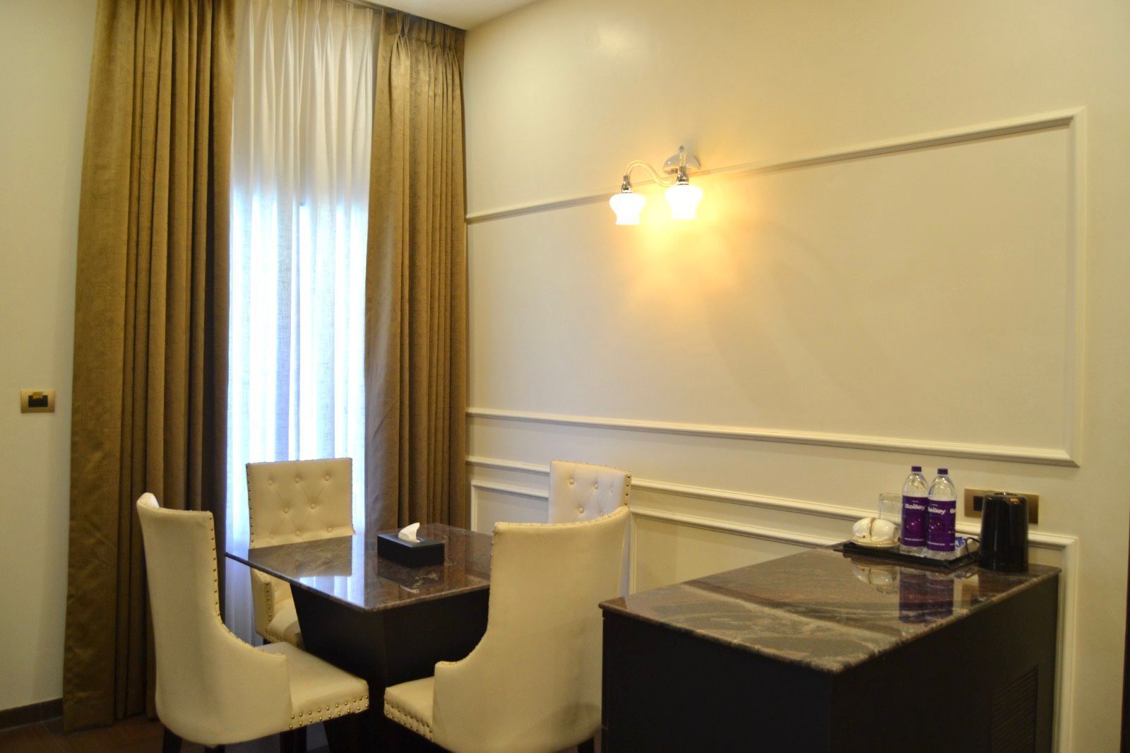 A hotel room with a dining table, two chairs, a tissue box, and a minibar with bottled water.