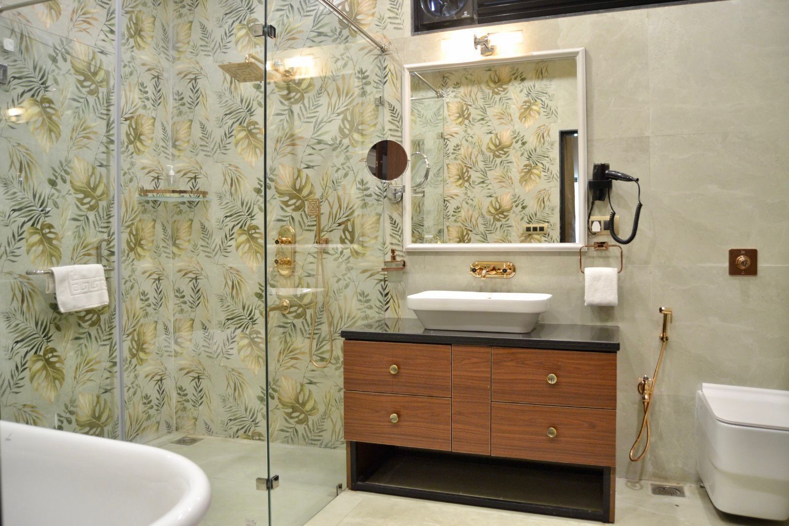 A bathroom with a glass shower enclosure, a white sink with a gold faucet, and a wooden vanity with drawers.