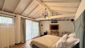 Quarto com cama, televisão, escrivaninha e janela com cortinas.
