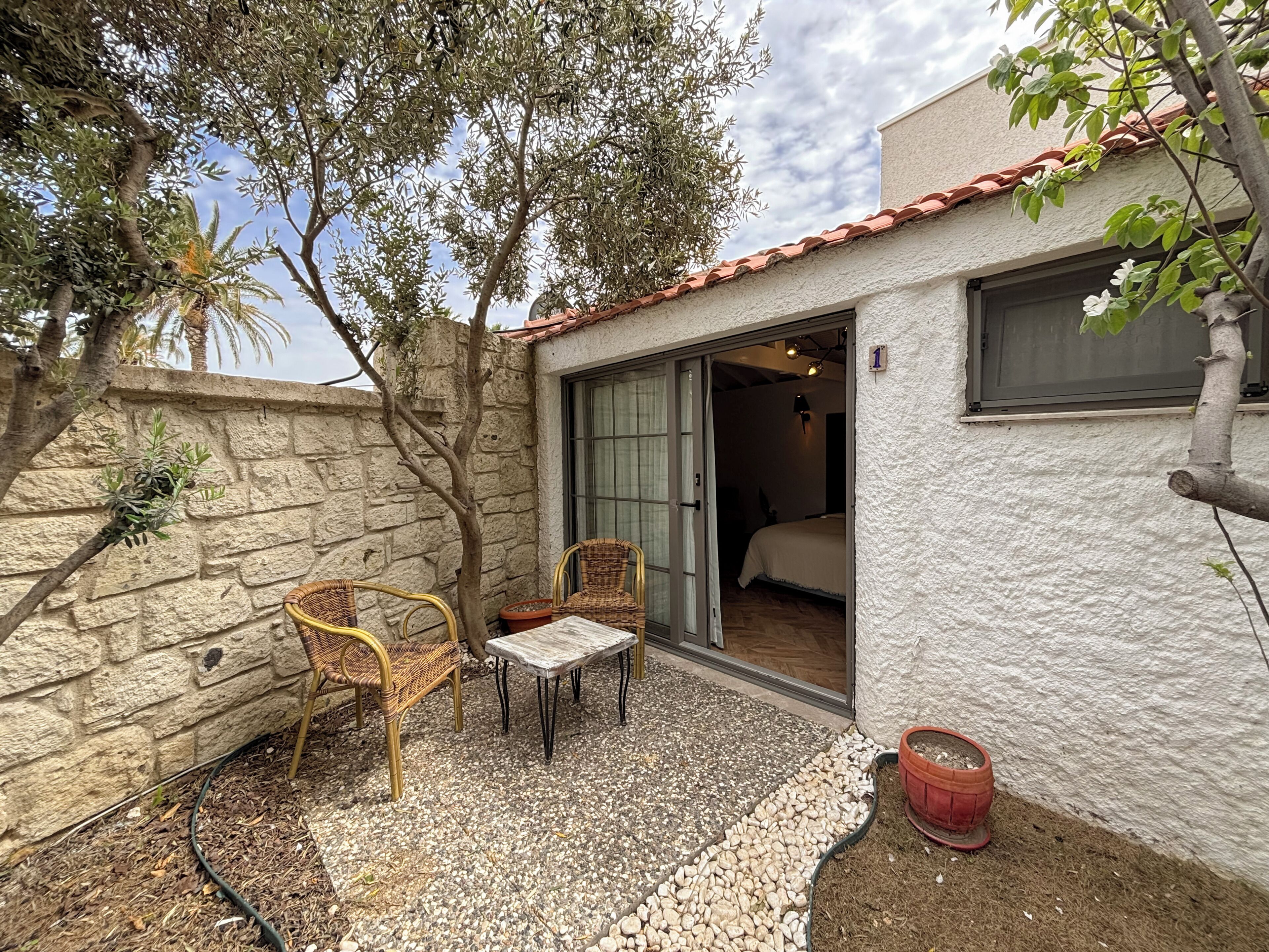 A small, private villa with a stone wall, a patio with wicker furniture, and a bedroom with a bed and a window.