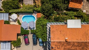 An aerial view of a residential area with a swimming pool, parked cars, and a rooftop with a solar panel. - Holiday Home Regina (Sibenik)