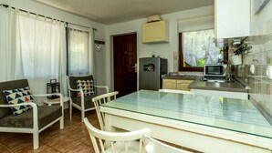 A compact kitchen with a refrigerator, microwave, and sink. There is a dining area with a glass table and white chairs. - Holiday Home Regina (Sibenik)