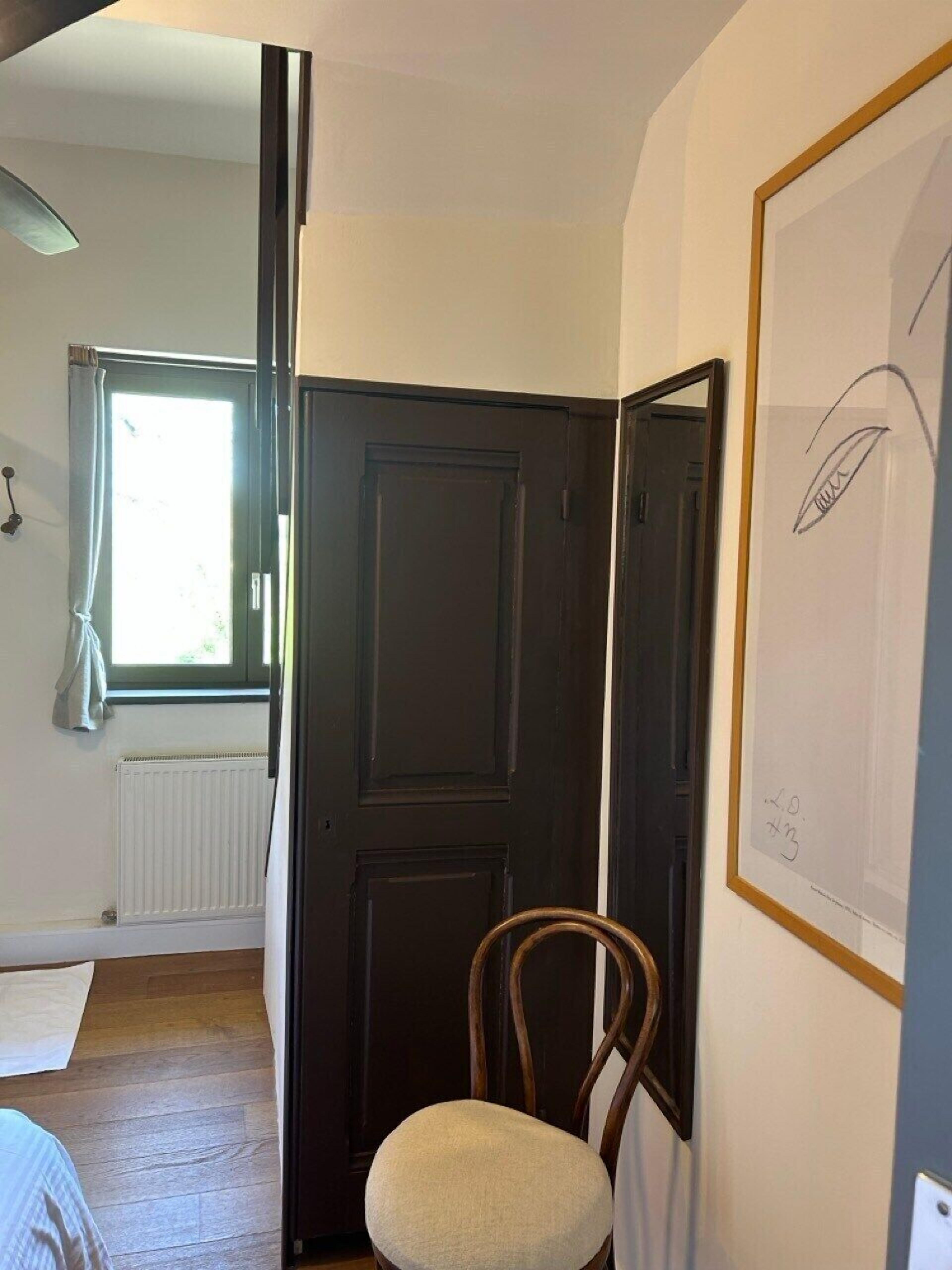 Une pièce avec un plancher en bois, une porte noire, un radiateur blanc et une fenêtre avec un rideau.