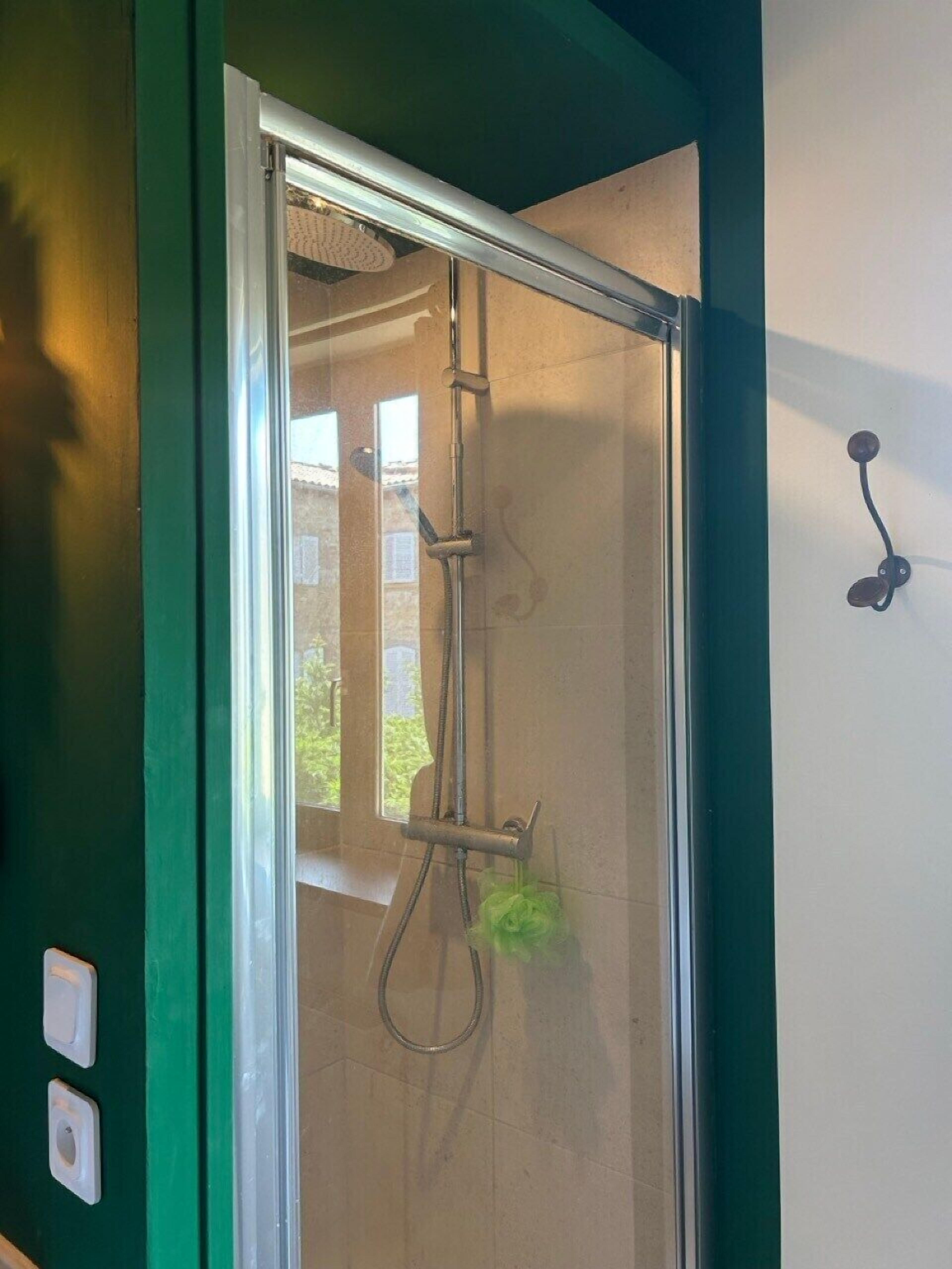 A shower with a glass door, a towel rack, and a wall-mounted light fixture.