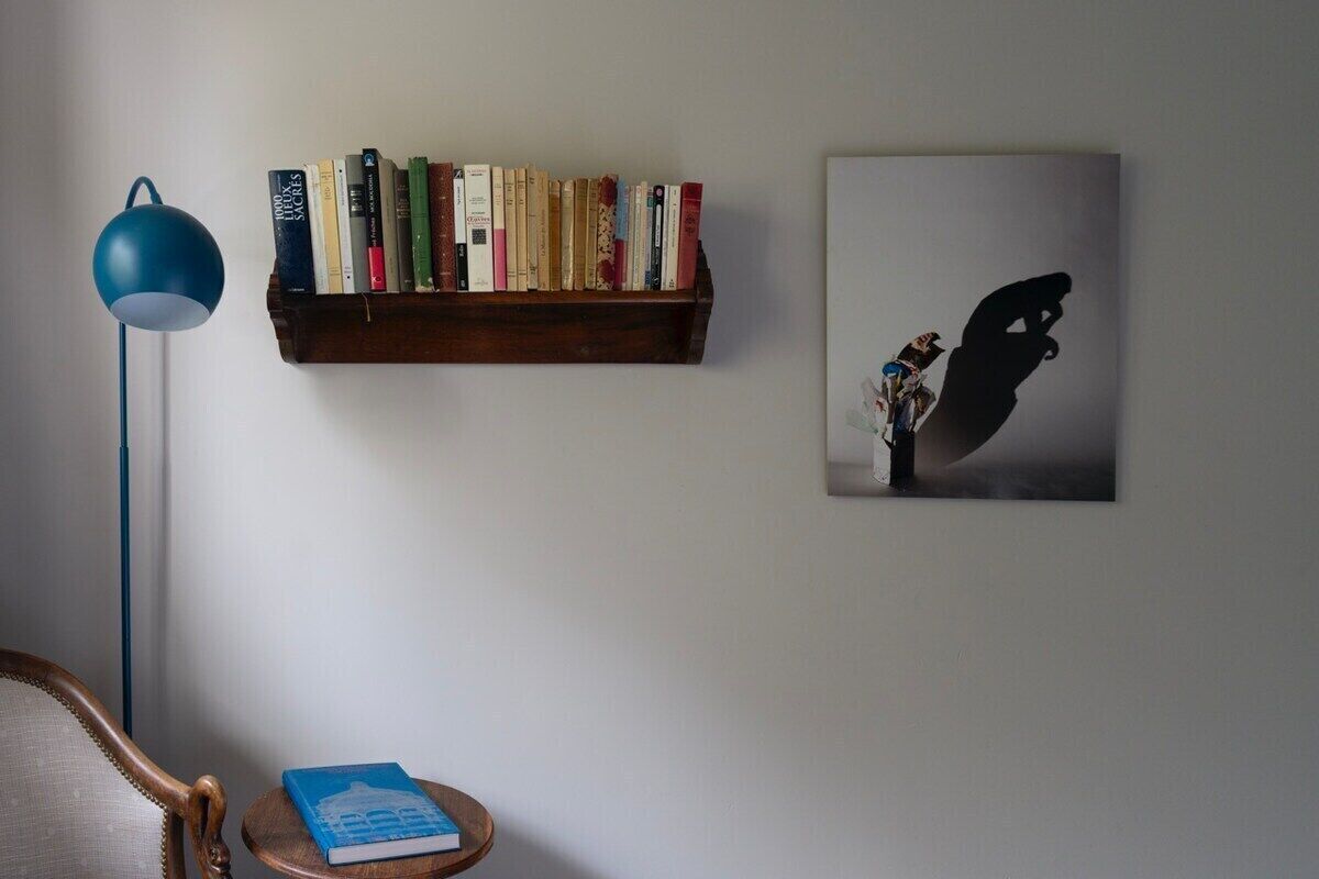 Una estantería con libros, una lámpara de pie azul, un sillón y una obra de arte enmarcada en la pared.