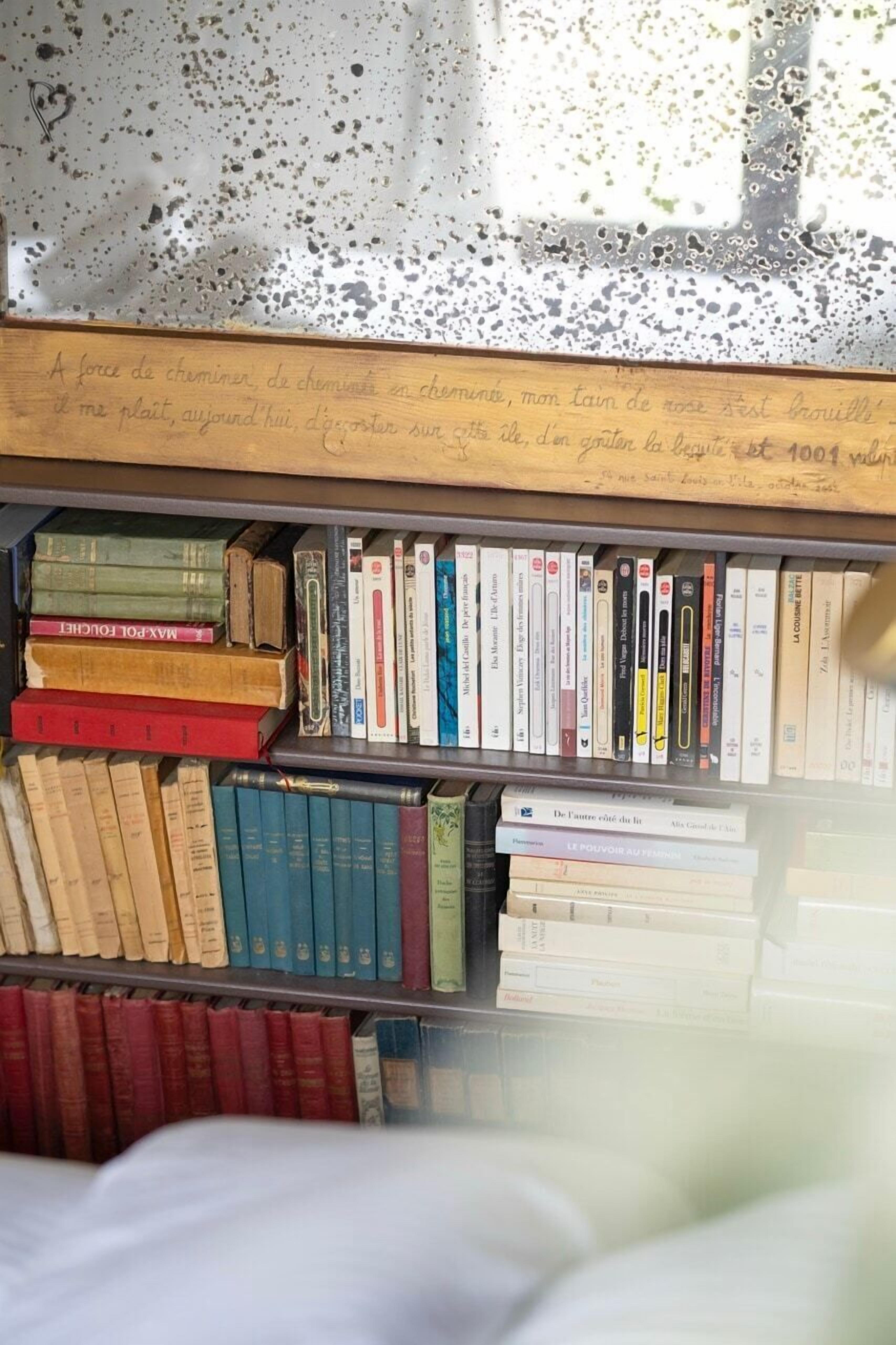 A bookshelf filled with books, a wooden plaque with text, and a lace curtain in the background.