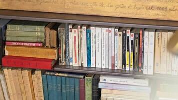 A bookshelf filled with books, a wooden plaque with text, and a lace curtain in the background.