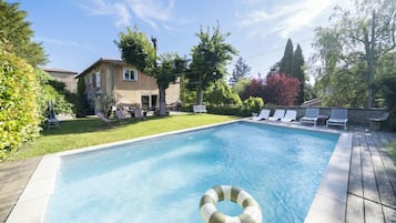 Una piscina con sillones de descanso y una casa al fondo.