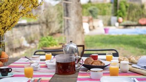 A breakfast setup with a table, tea pot, croissants, and orange juice on a colorful tablecloth. - La Rose du petit Bois (Saint-Didier-au-Mont-d'Or)
