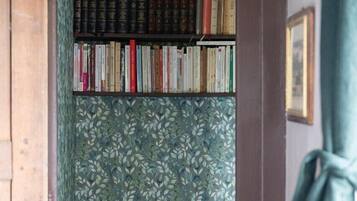 Een badkamer met een toilet, een boekenplank vol boeken en behang met een patroon.