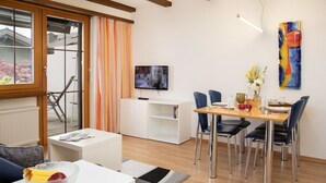 A modern living room with a dining area, a TV mounted on the wall, and a large window with curtains. - Cosy apartment for 4 people with pool, WIFI, TV, patio and panoramic view (Falera)