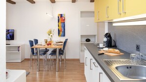 A modern kitchen with a central island, a dining area with chairs, and a TV mounted on the wall. - Cosy apartment for 4 people with pool, WIFI, TV, patio and panoramic view (Falera)