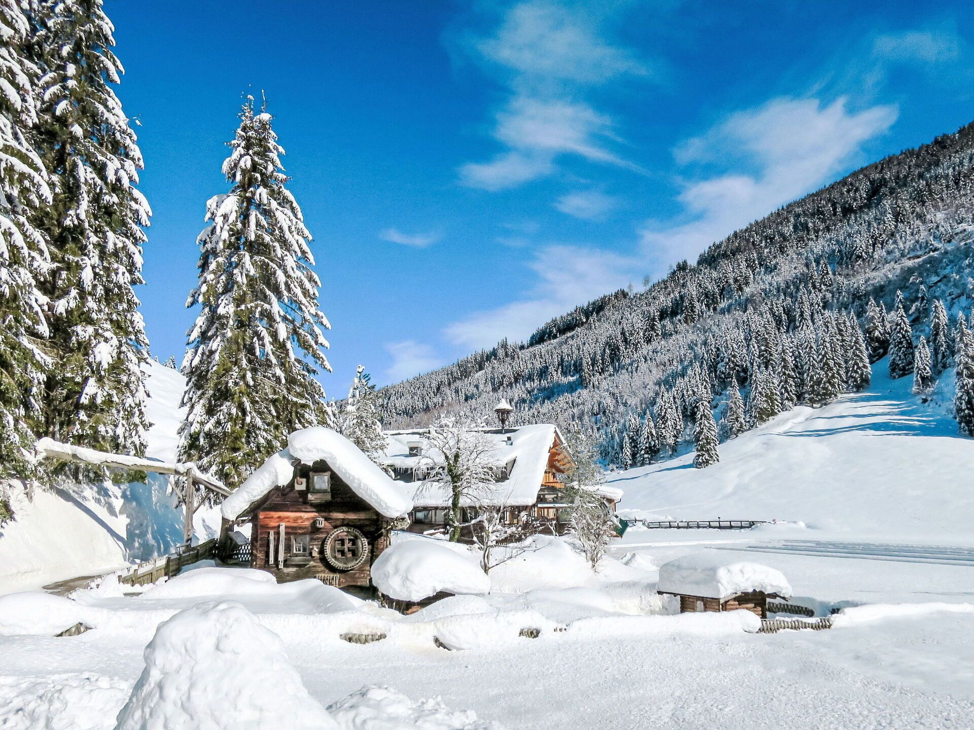 A snow-covered lodge with a wooden exterior, surrounded by snow-laden trees and a mountainous backdrop.