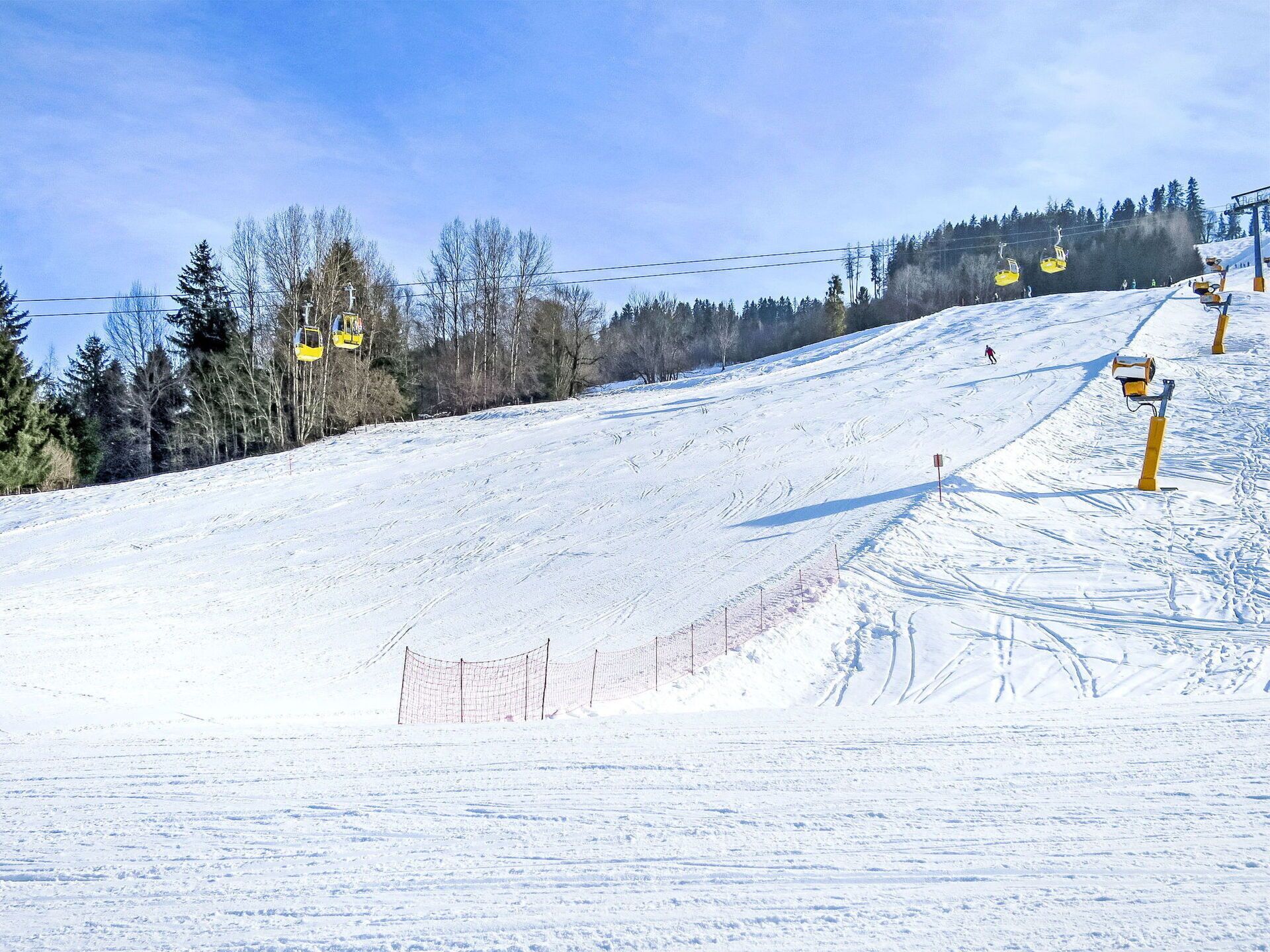 A snowy ski slope with a chairlift, trees, and a clear sky.